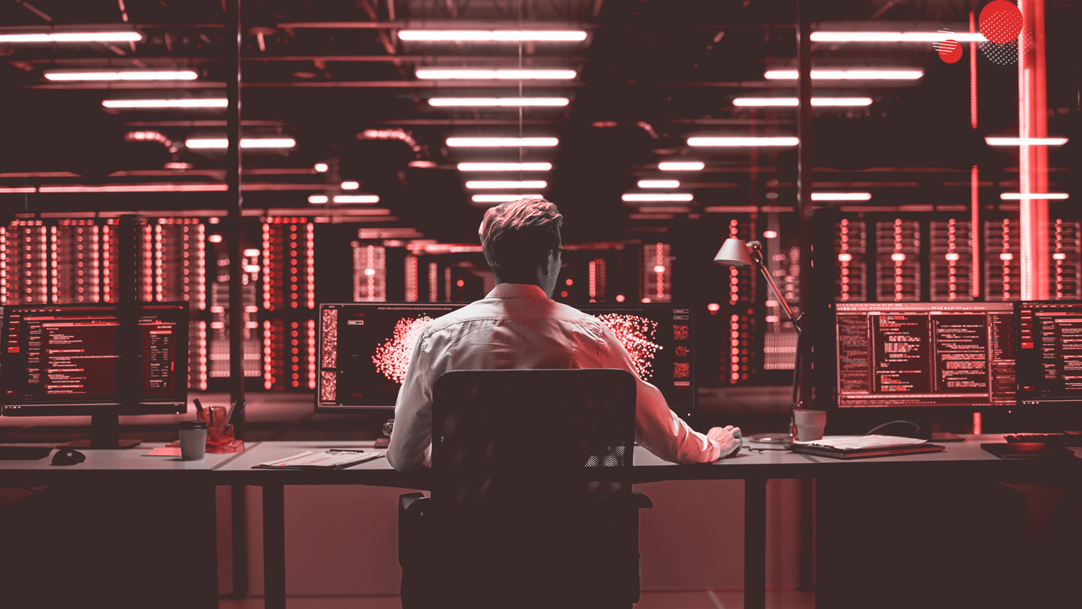 Um administrador de sistemas sentado de costas para a câmera, trabalhando em um ambiente de data center iluminado por luzes vermelhas. Ele está rodeado por vários monitores exibindo gráficos complexos e dados de servidores, refletindo a intensidade e a complexidade do gerenciamento de servidores modernos.