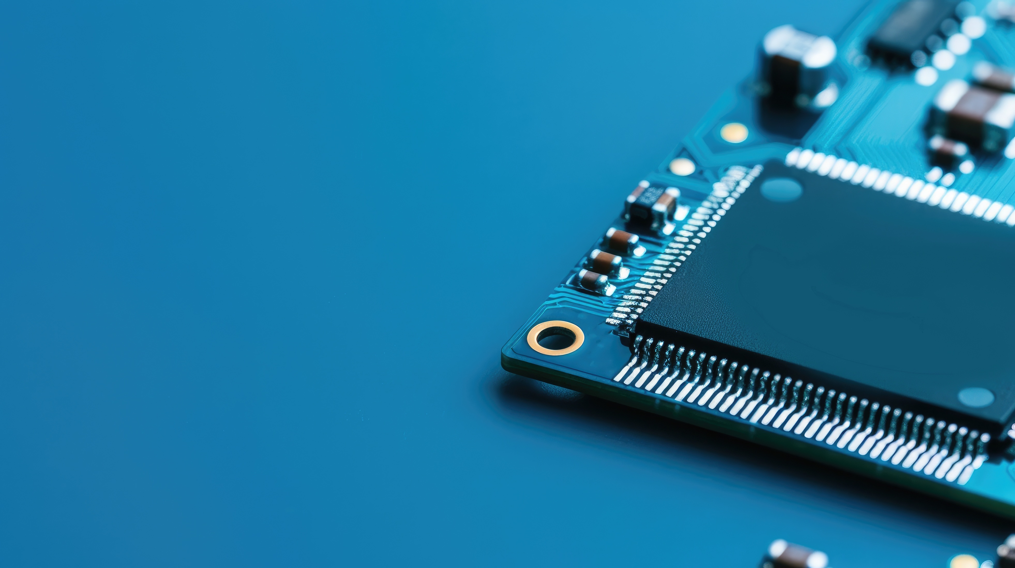 Macro de uma placa de circuito azul-petróleo em ângulo, com um chip quadrado escuro e pinos de solda prateados à direita.