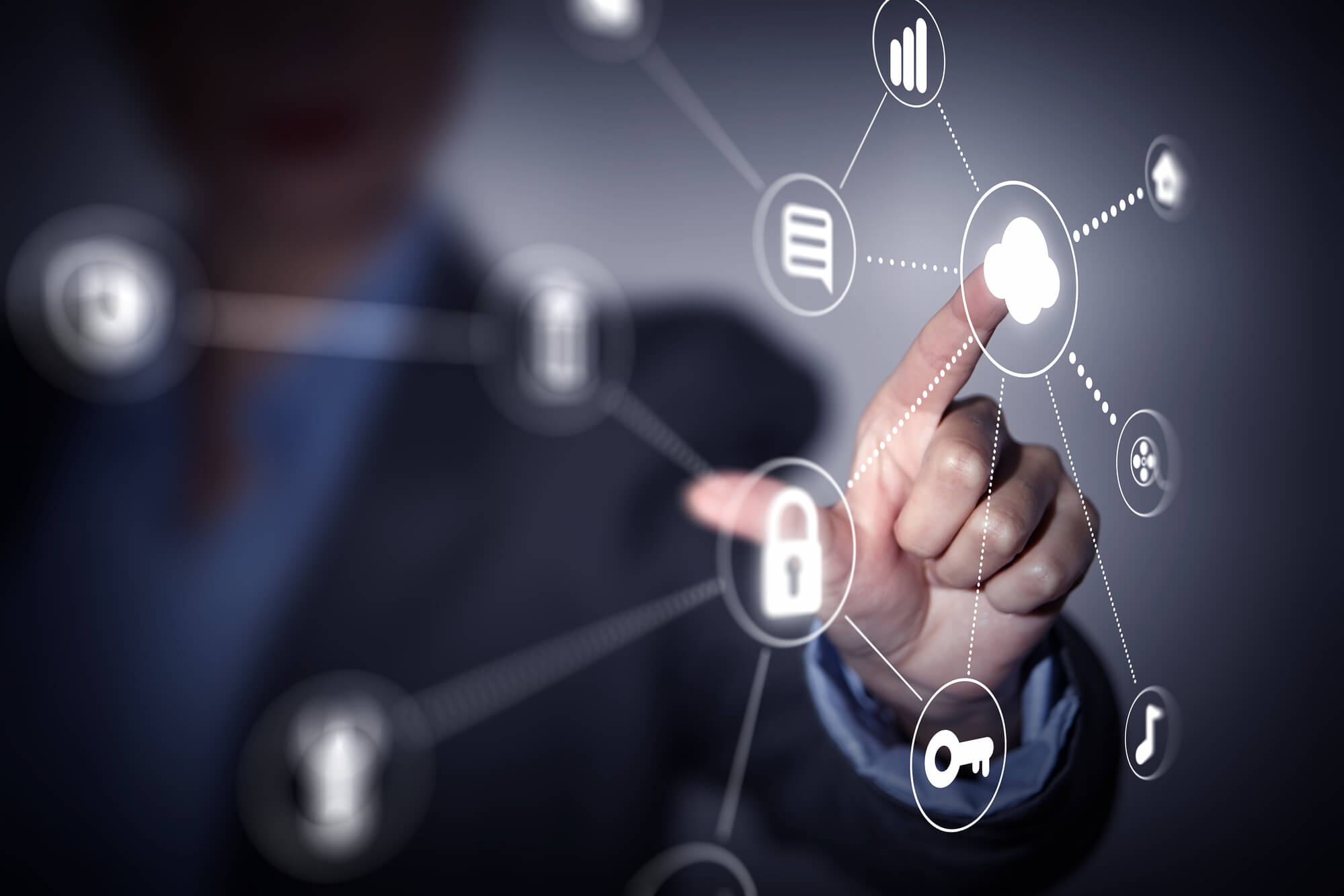 Uma mão toca uma tela transparente com vários ícones de computação em nuvem, representando nuvens híbrida, pública e privada. O fundo é desfocado e escuro, destacando os ícones interconectados e a interação da mão com eles, evidenciando as diferenças entre os tipos de nuvem.
