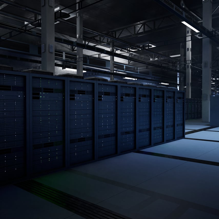 A imagem mostra o interior de um data center moderno, com uma longa fileira de racks de servidores alinhados em um ambiente amplo e industrial. Os racks são altos, escuros (em tons de azul e preto) e apresentam luzes de status discretas em verde e azul, indicando os equipamentos em operação. O espaço é bem organizado e limpo, com piso elevado típico de data centers, usado para passagem de cabos e controle de refrigeração. No teto, há uma estrutura metálica exposta com dutos, vigas e sistemas de iluminação, reforçando o caráter técnico e robusto da instalação. A iluminação é baixa e fria, criando uma atmosfera de alta tecnologia e operação contínua. No conjunto, a imagem transmite a ideia de infraestrutura crítica, associada a computação em nuvem, processamento de dados em larga escala, inteligência artificial ou ambientes corporativos de missão crítica.
